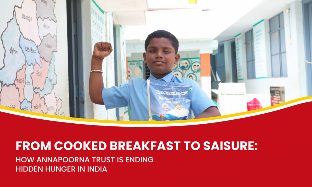 A schoolboy in a blue uniform raises his fist while holding a SaiSure nutrition packet in a government school corridor.